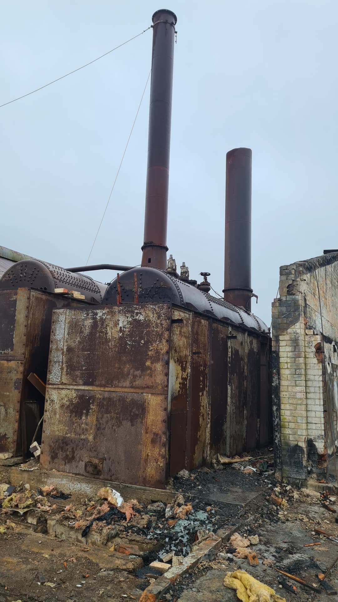 Rusted industrial boilers and flues left standing among fire-damaged brickwork