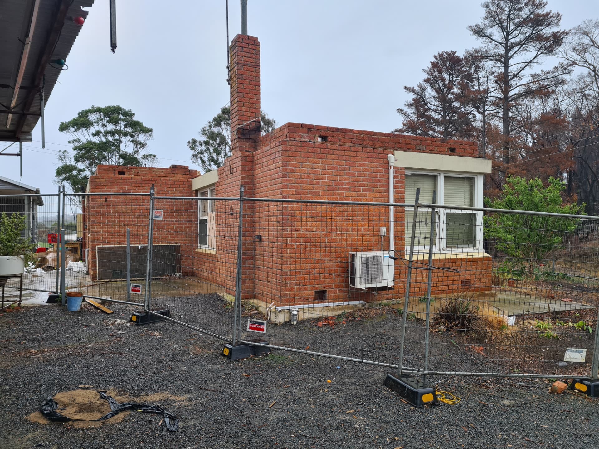 Fire-damaged brick house behind temporary safety fencing awaiting clearance